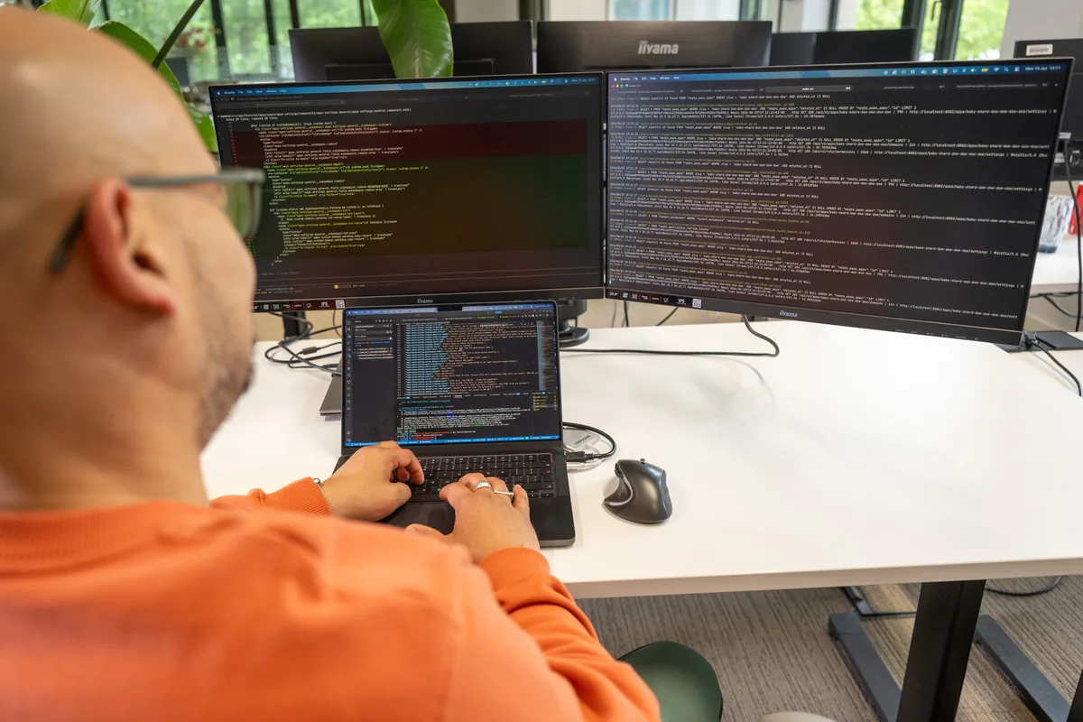 Ontwikkelaar met dubbele monitors en laptop, veel schermen met code